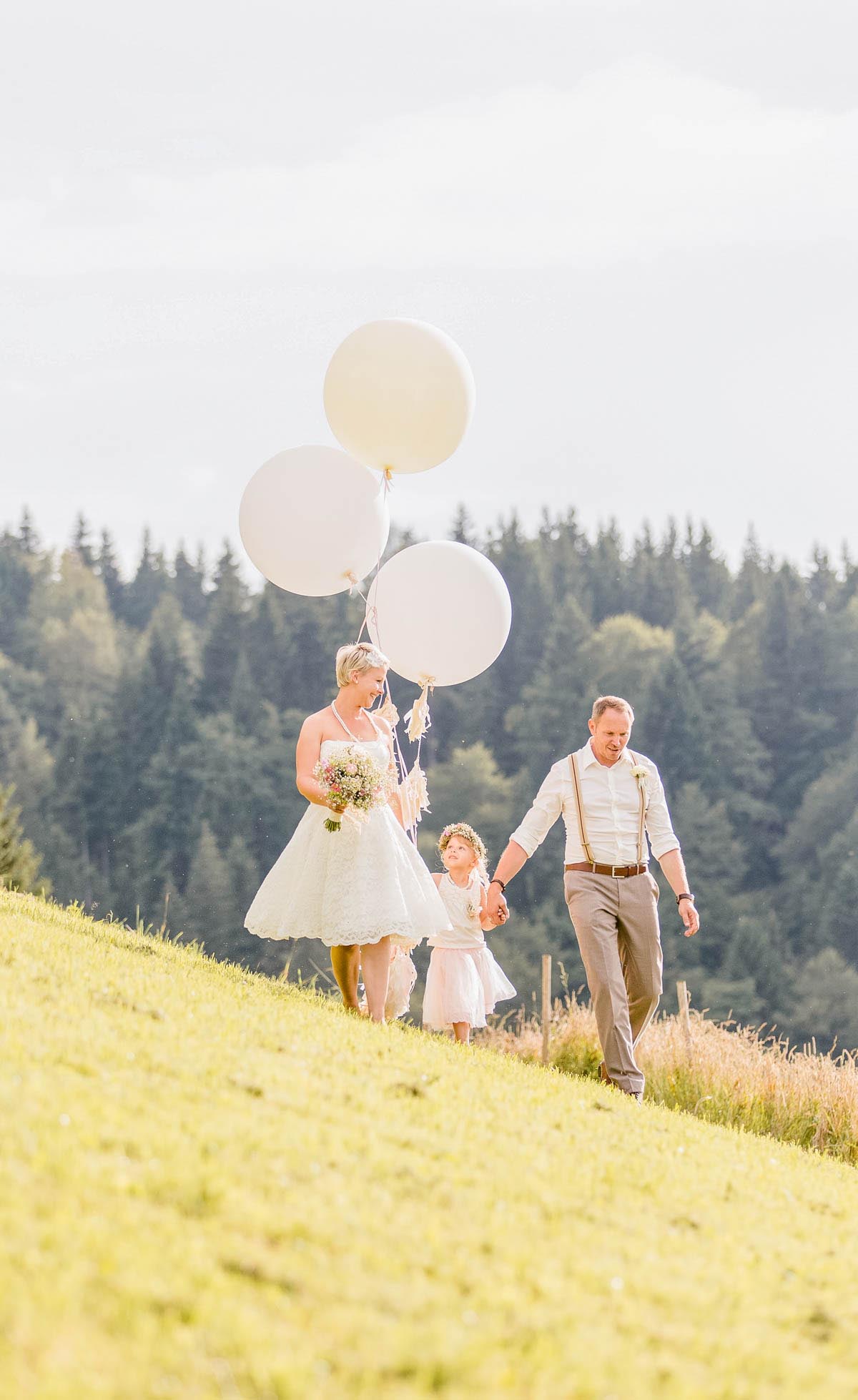 Brautpaar mit weißen Luftballons auf der Almwiese