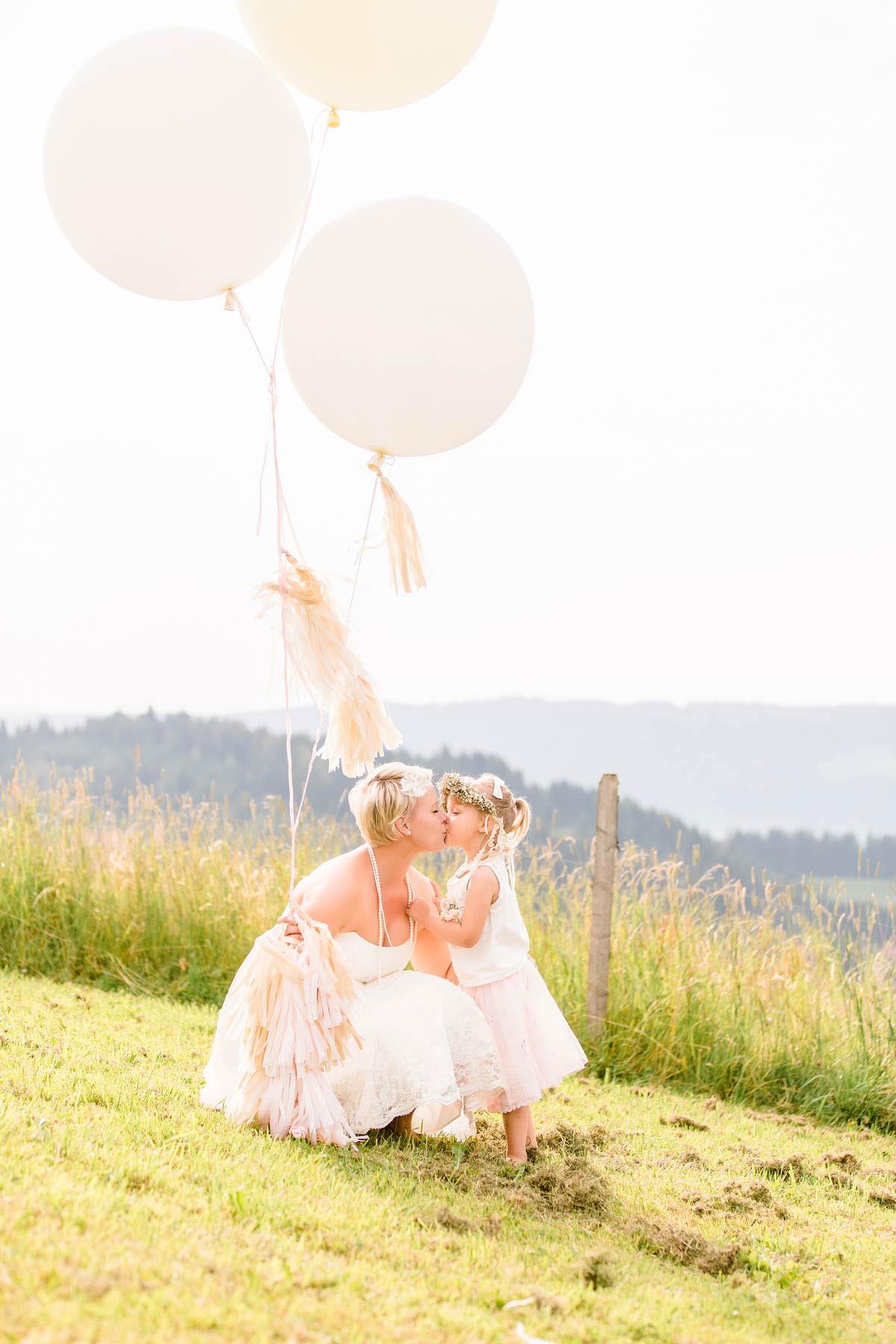 Brautpaar mit Luftballons sitzt auf der Wiese mit Blick ins Tal