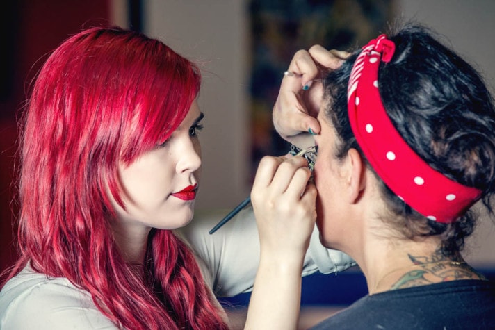 Visagistin schminkt die Braut, die ein rotes Tuch mit weißen Punkten im Haar trägt