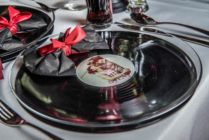 Gedeckter Tisch mit Schallplatte als Platzteller, schwarzer Serviette und roter Schleife