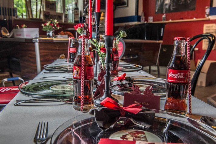 Hochzeitstafel mit Coca-Cola-Glasflaschen, roten Kerzen und schwarzen Tellern