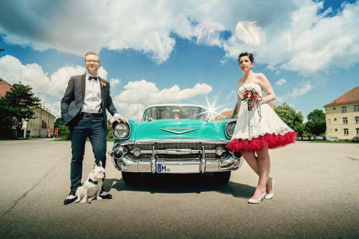Brautpaar mit Hund vor dem türkisfarbenen Oldtimer unter blauem Himmel