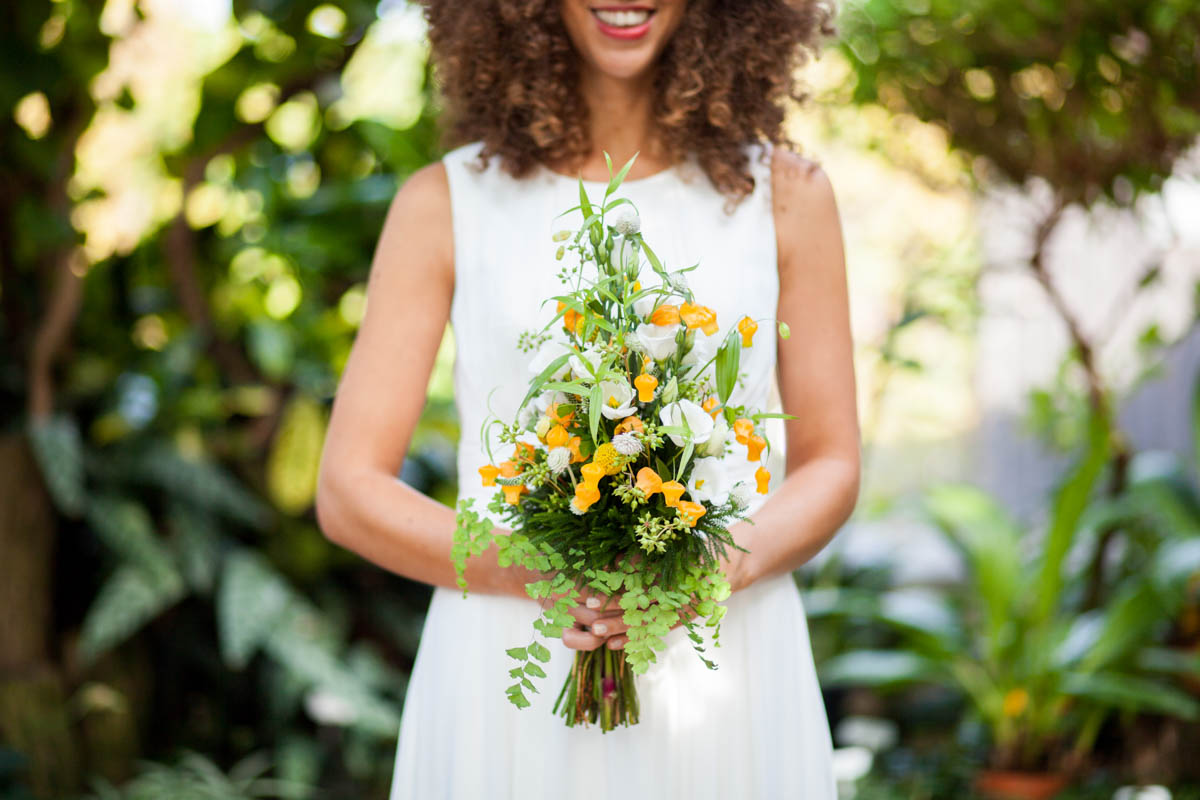 Braut im schlichten weißen Kleid hält einen Strauß mit orangefarbenen und weißen Blüten