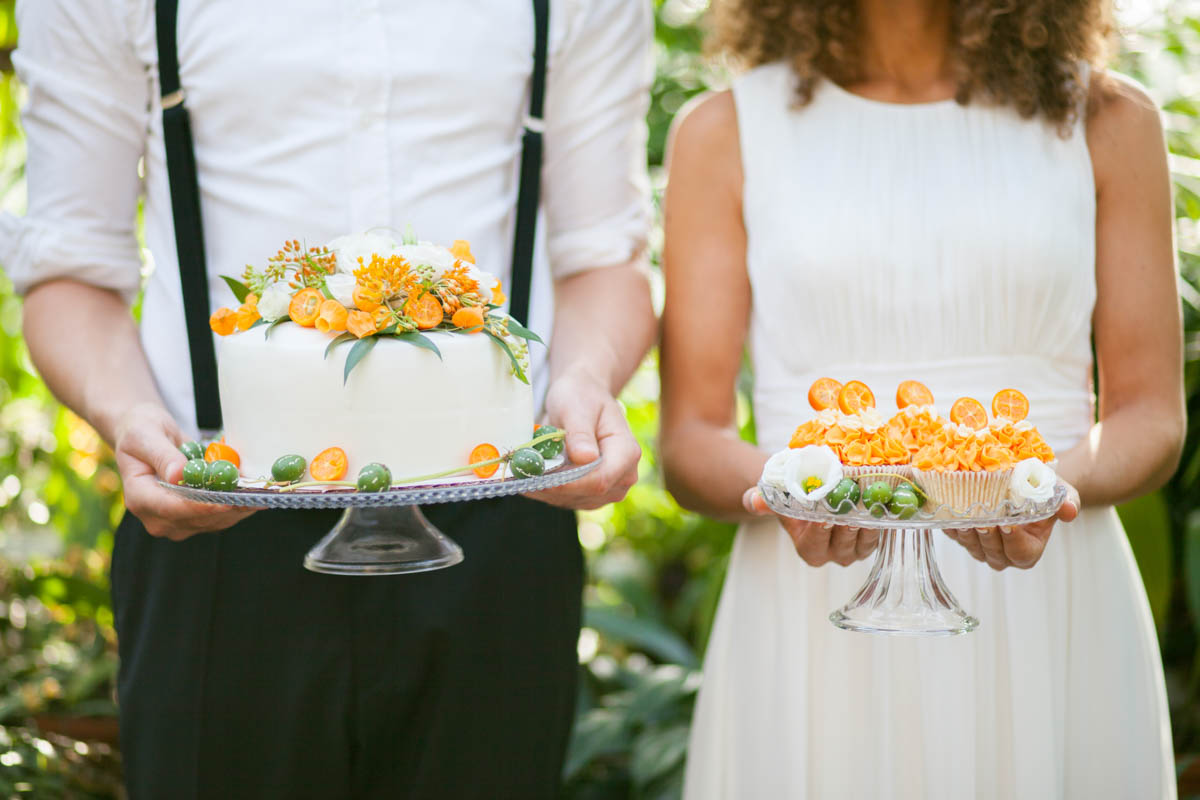 Brautpaar hält jeweils eine kleine Torte mit orangefarbenen Blüten in den Händen