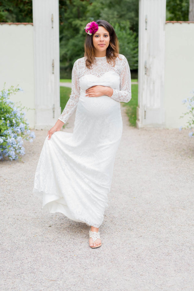 Schwangere Braut läuft im langen Spitzenkleid über einen Kiesweg und rafft den Rock