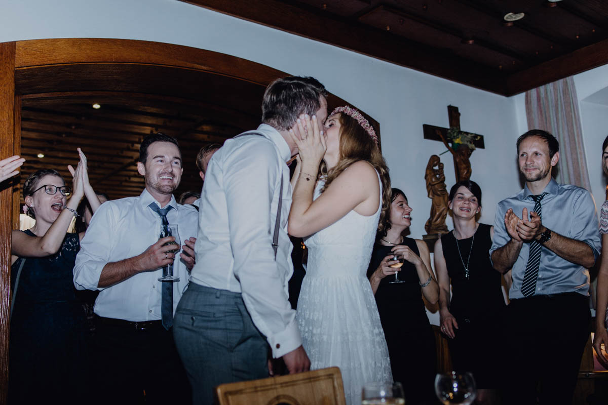 küssendes Brautpaar vor Hochzeitsgesellschaft