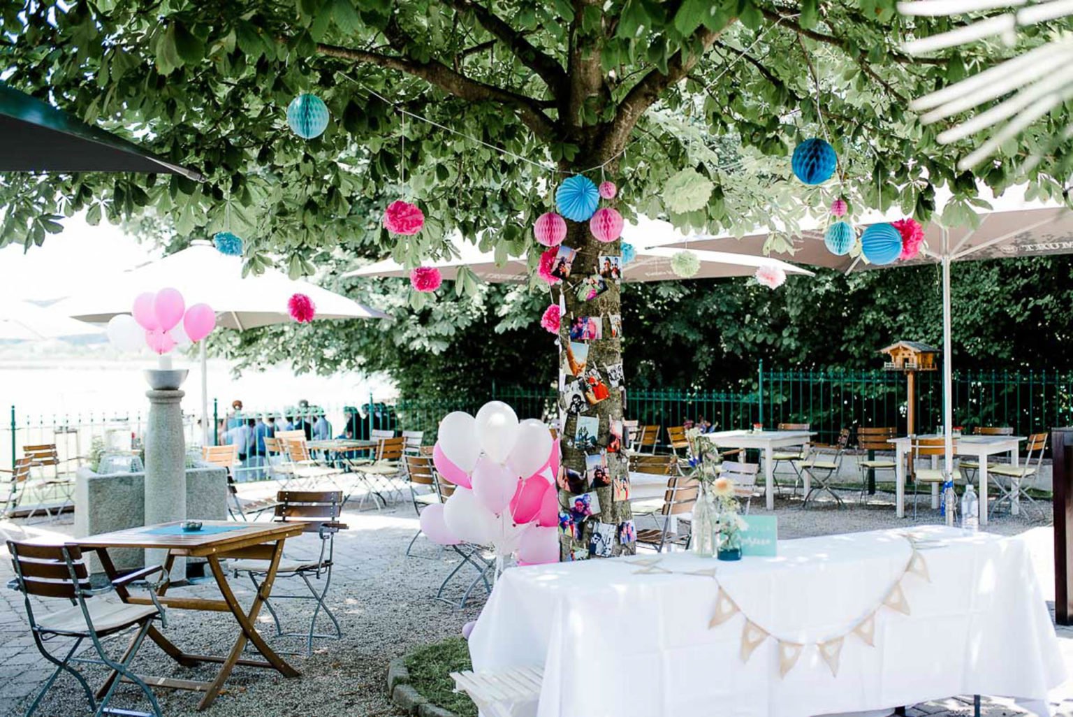 Garten am See mit Lampions, Wimpelketten und Luftballons unter einem großen Baum