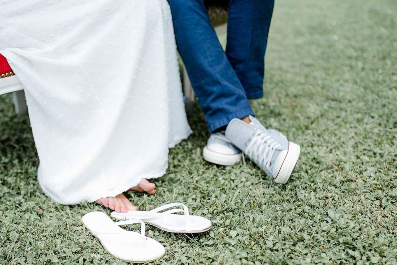 Füße des Brautpaares: weiße Sneaker und abgestreifte Flip-Flops im Gras