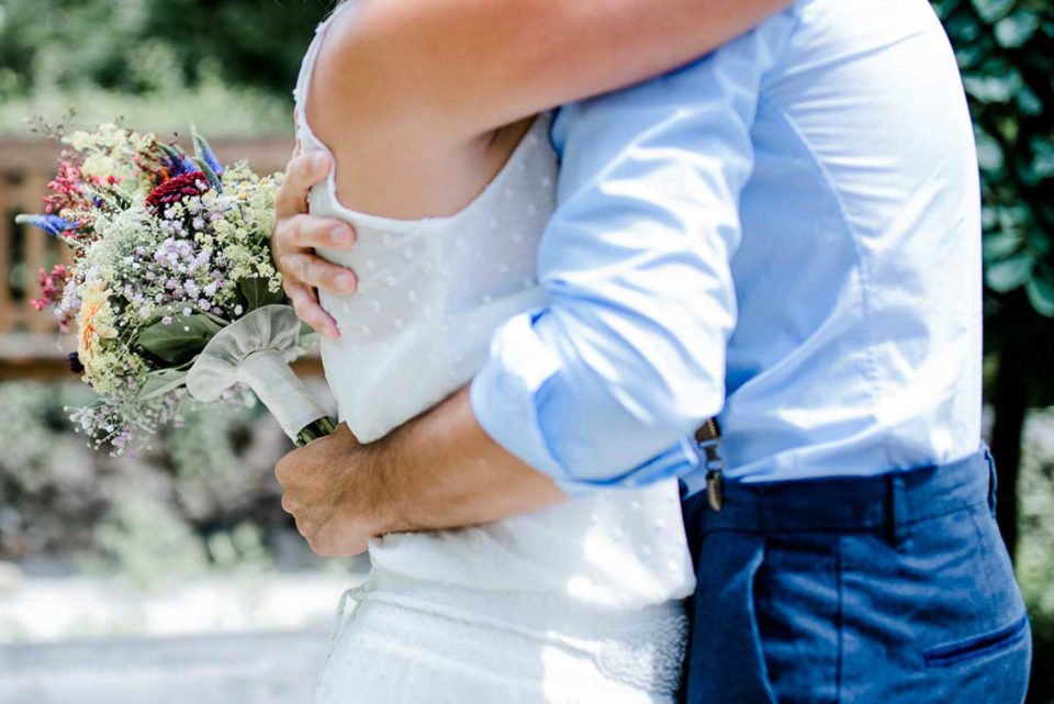 Bräutigam umarmt Braut und hält Brautstrauß