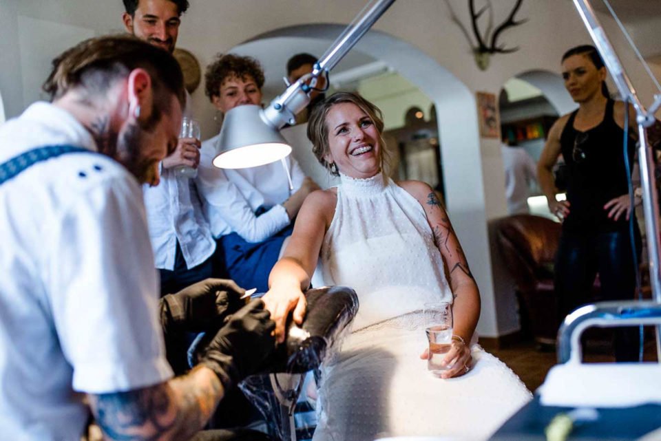 Braut lacht während sie ihren Ehering an der Hochzeit tätowiert bekommt