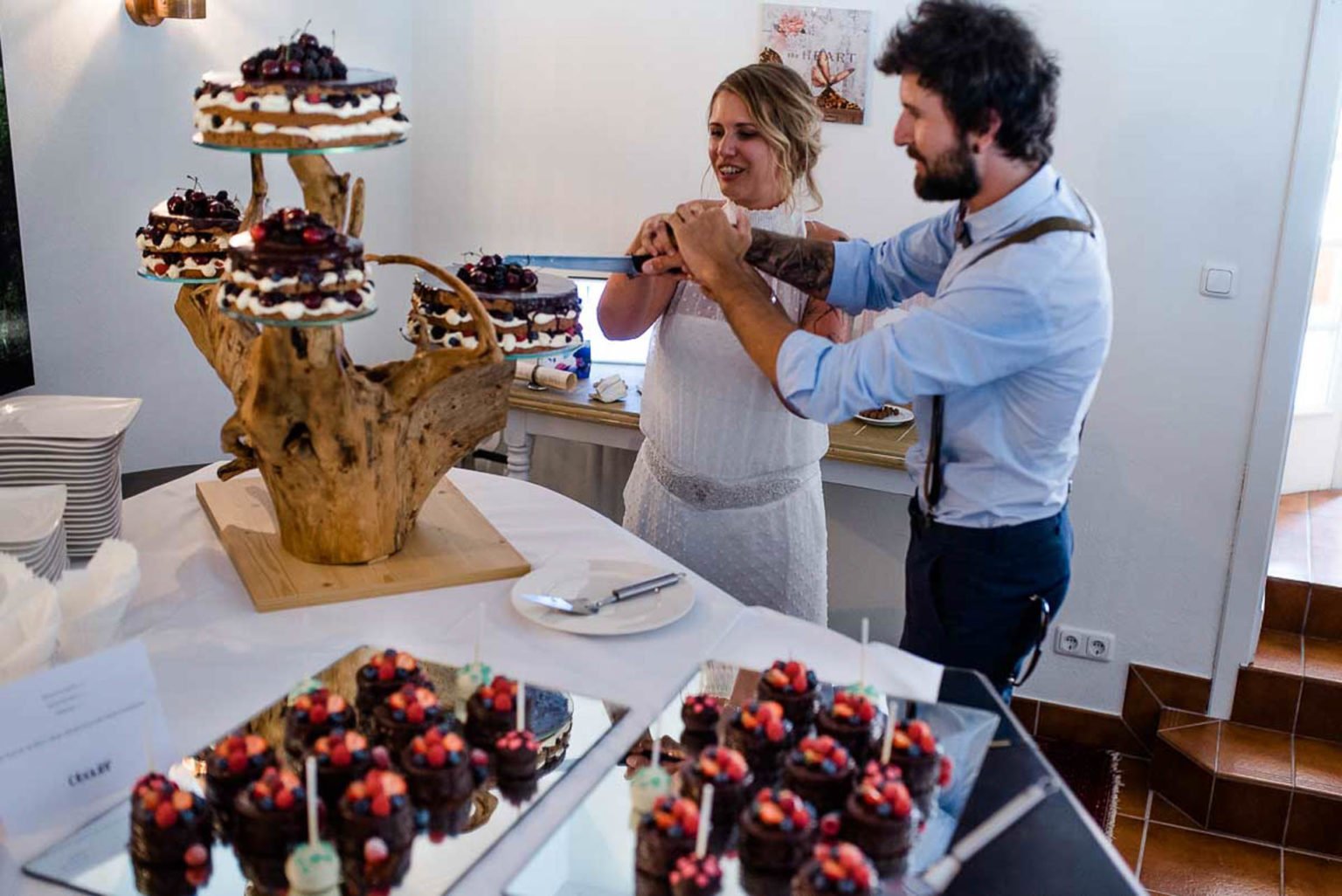Brautpaar schneidet die Hochzeitstorte an, daneben kleine Schokotörtchen mit Beeren