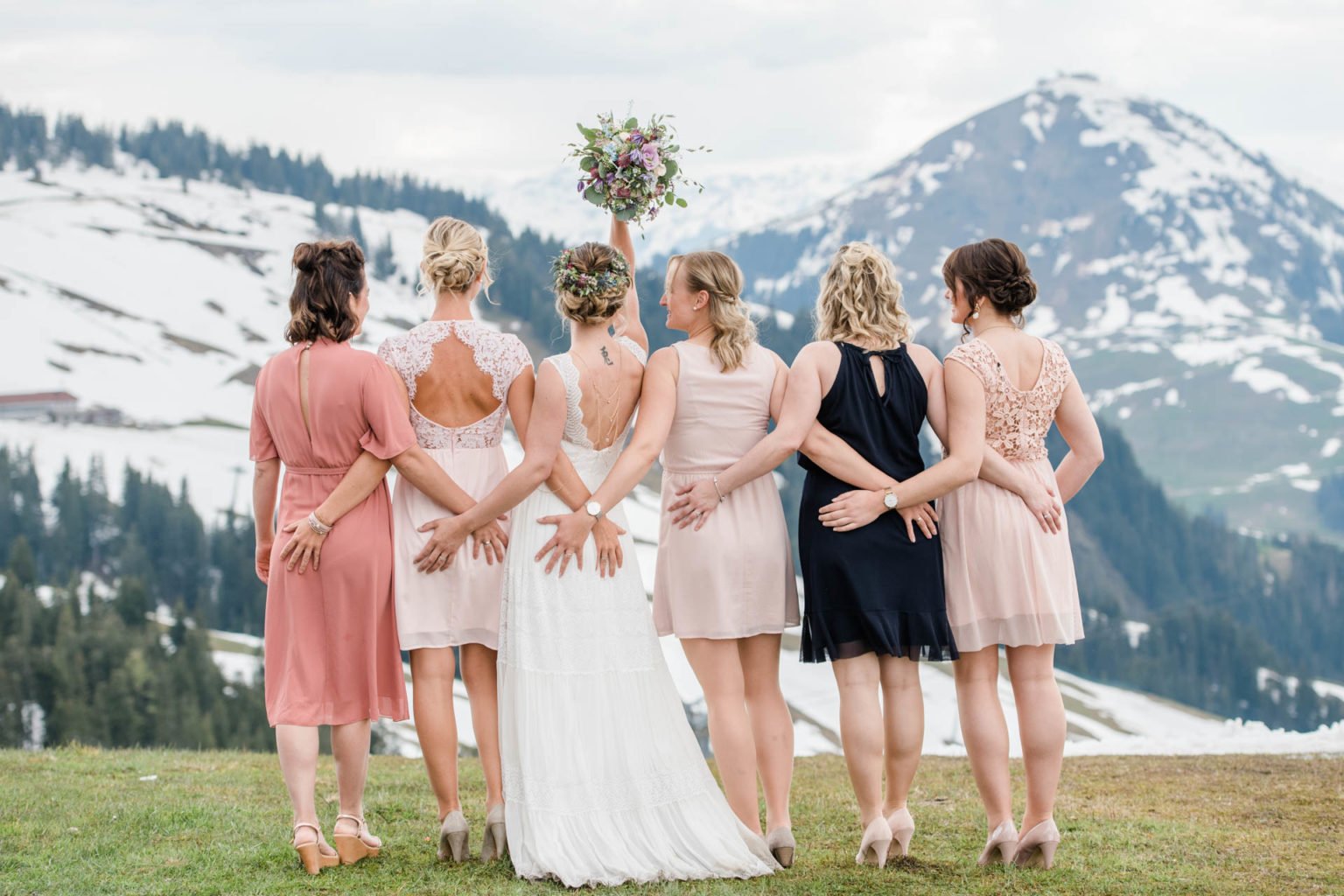 Braut und Brautjungfern in Rosétönen von hinten vor verschneiten Bergen