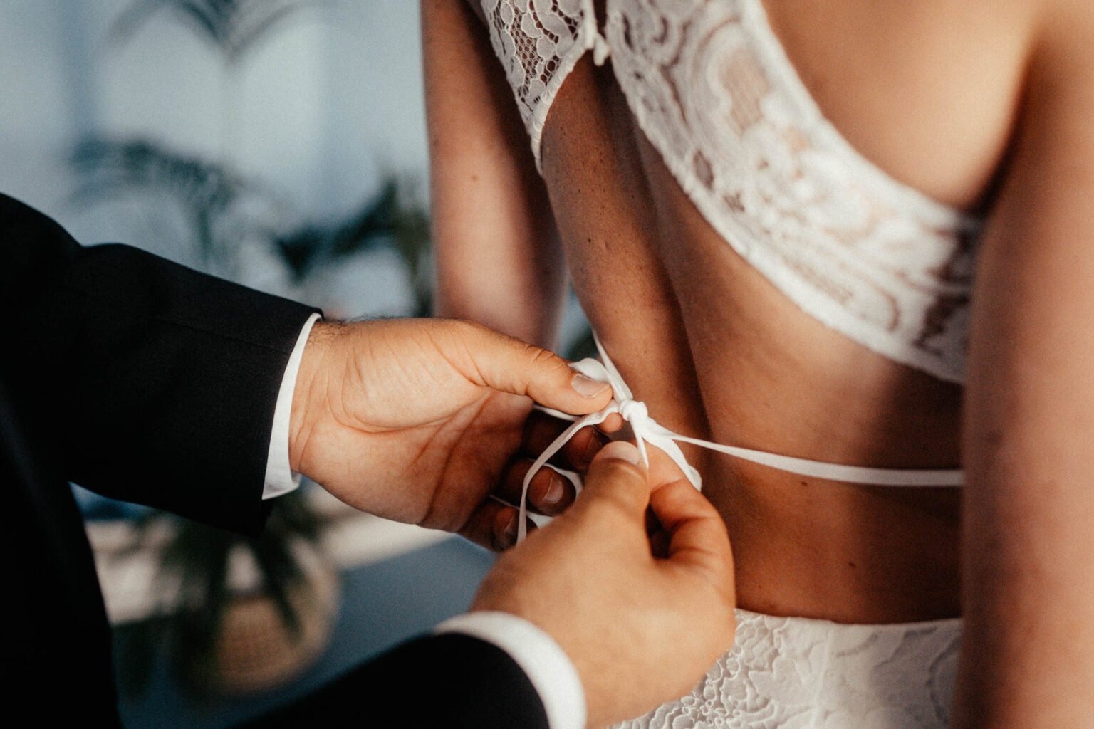Bräutigam schließt das Band am rückenfreien Spitzenkleid der Braut