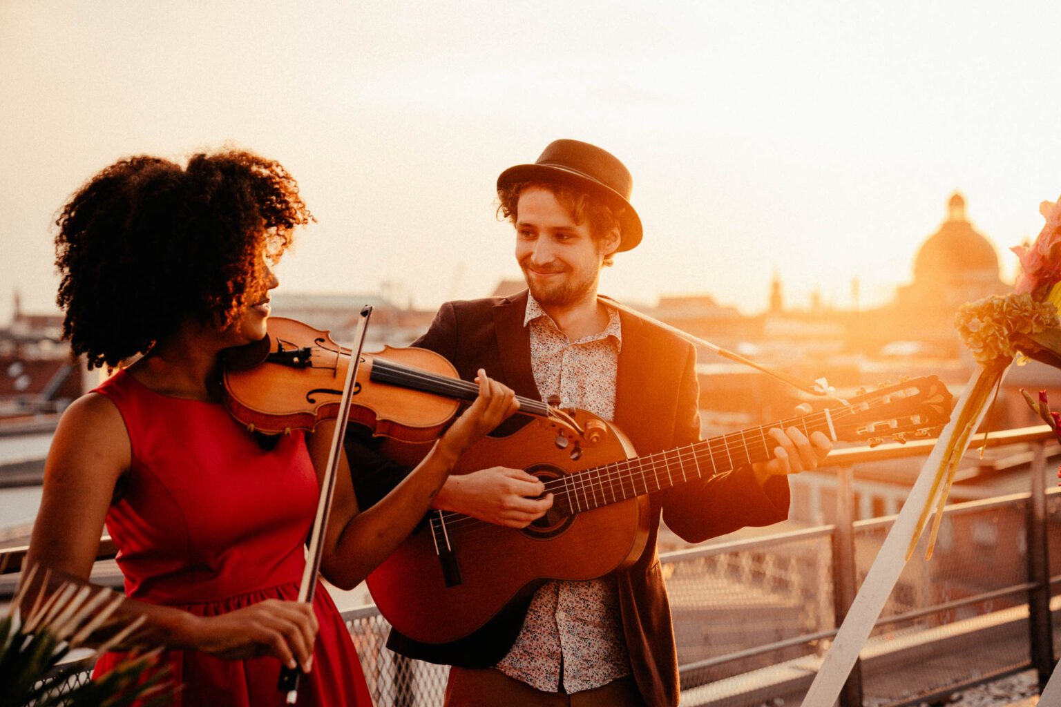 Musikerin mit Geige und Musiker mit Gitarre spielen im Gegenlicht auf der Dachterrasse
