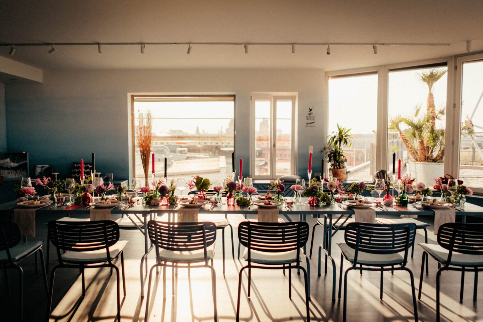 Lange Hochzeitstafel mit pinken Kerzen und Blumen in einem hellen Loft mit großen Fenstern