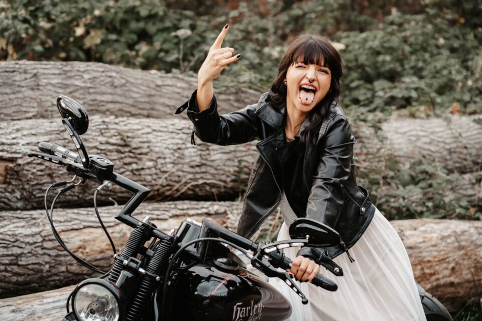 Braut im Zweiteiler mit Lederjacke auf Motorrad freut sich und streckt die Zunge raus