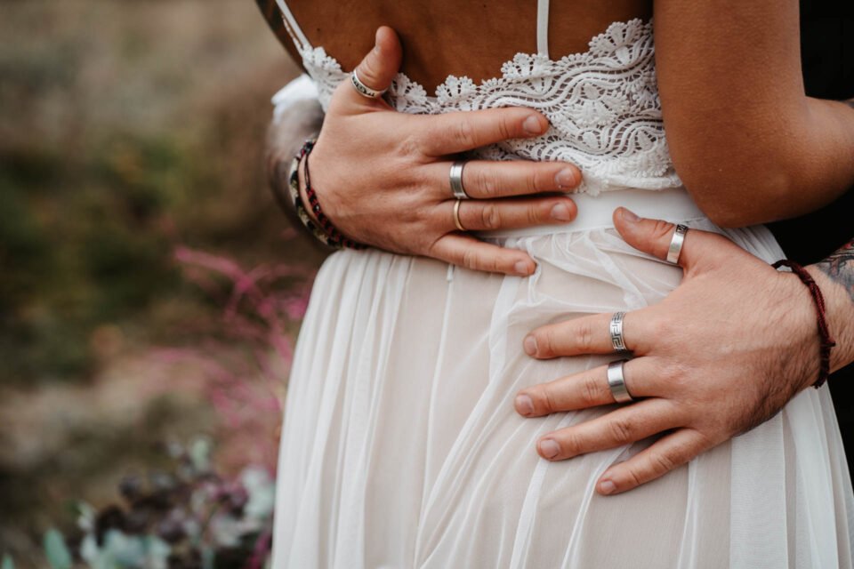 Detailaufnahme: Bräutigam mit vielen Ringen umarmt seine Braut an der Hüfte