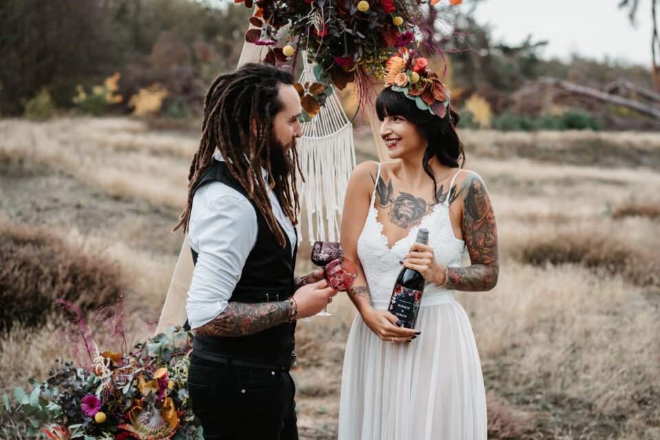Tätowiertes Brautpaar am Waldrand mit Gläsern und Wein