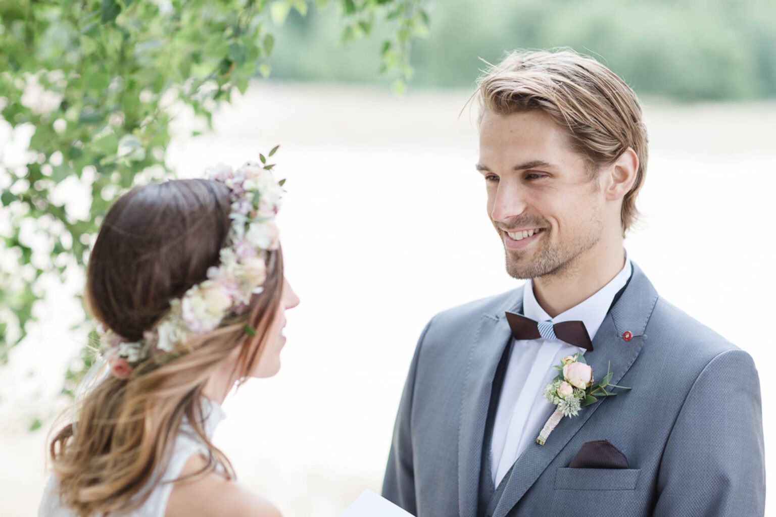 Braut mit Blumenkranz lacht ihren Bräutigam an