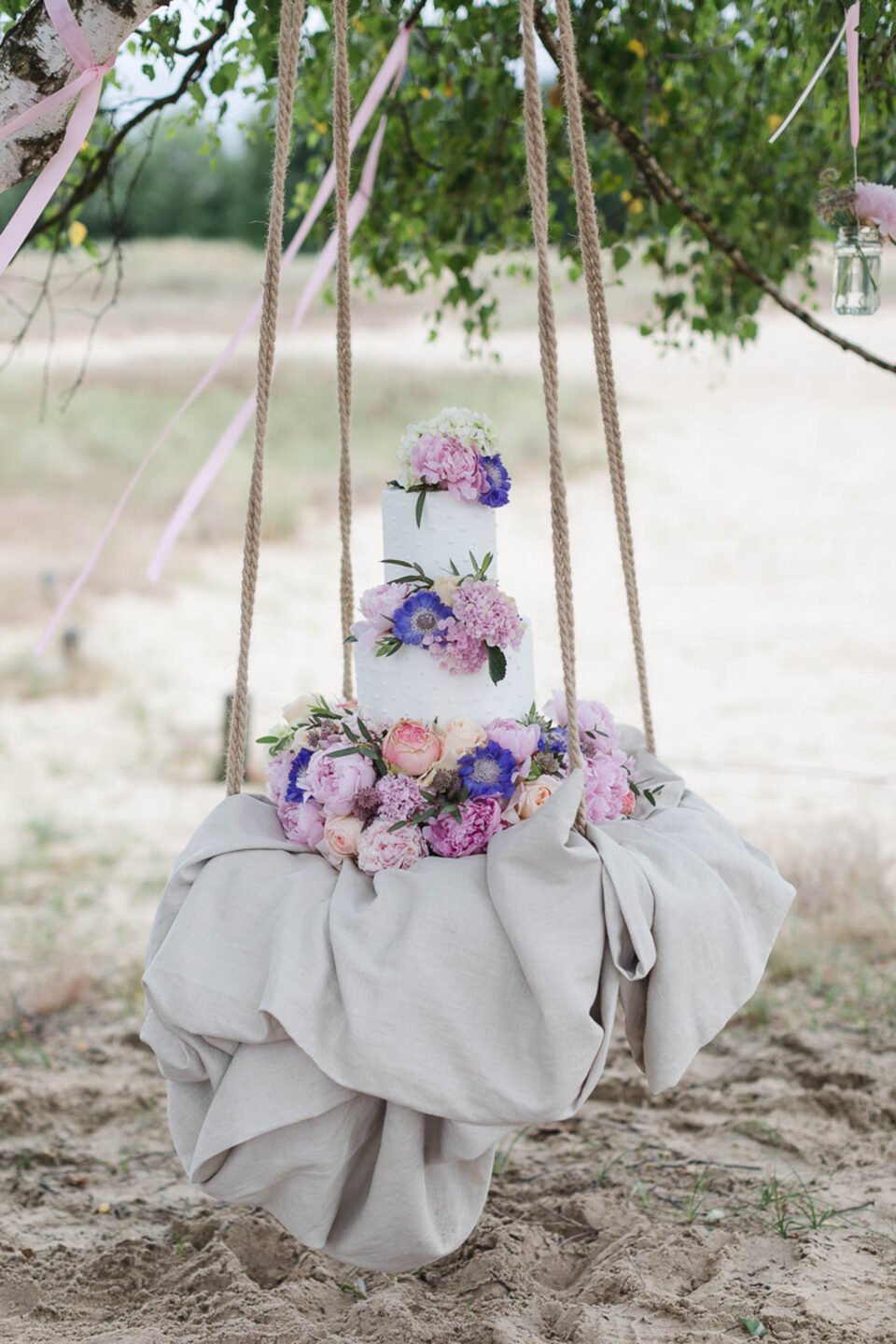 Dreistöckige Hochzeitstorte mit Blumen auf einer Schaukel