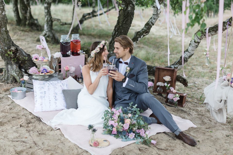Brautpaar stößt auf sich an nach der romantischen Trauung unter Bäumen