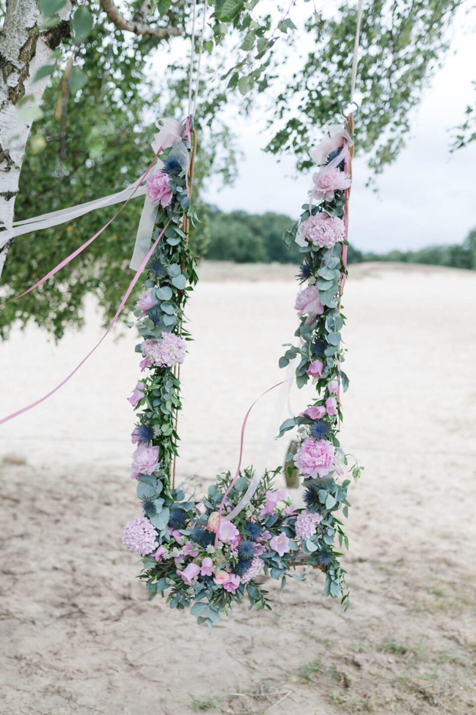 Schaukel mit Blumendeko für romantische Trauung unter Bäumen