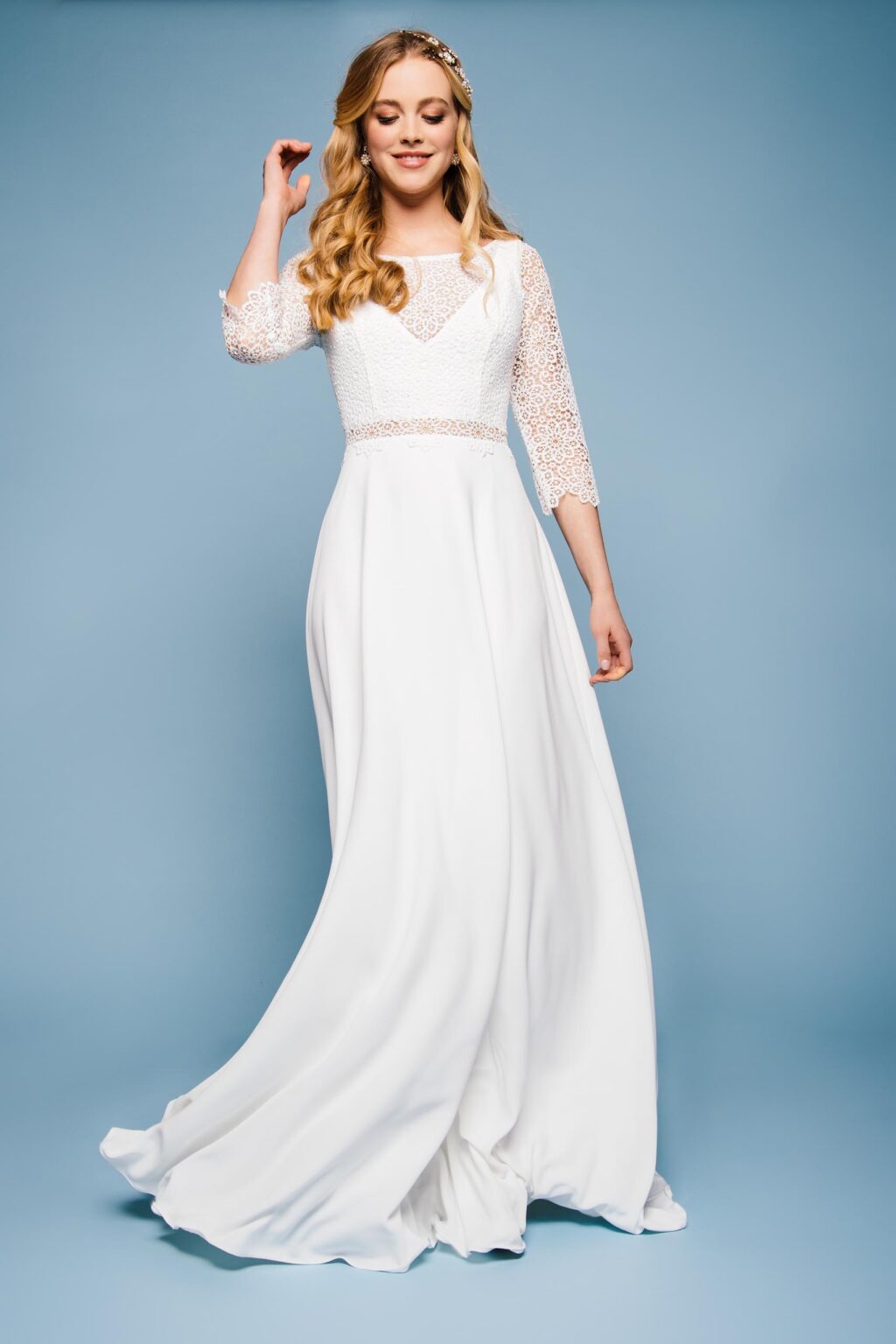Braut im Spitzenkleid mit langen transparenten Ärmeln vor blauem Hintergrund