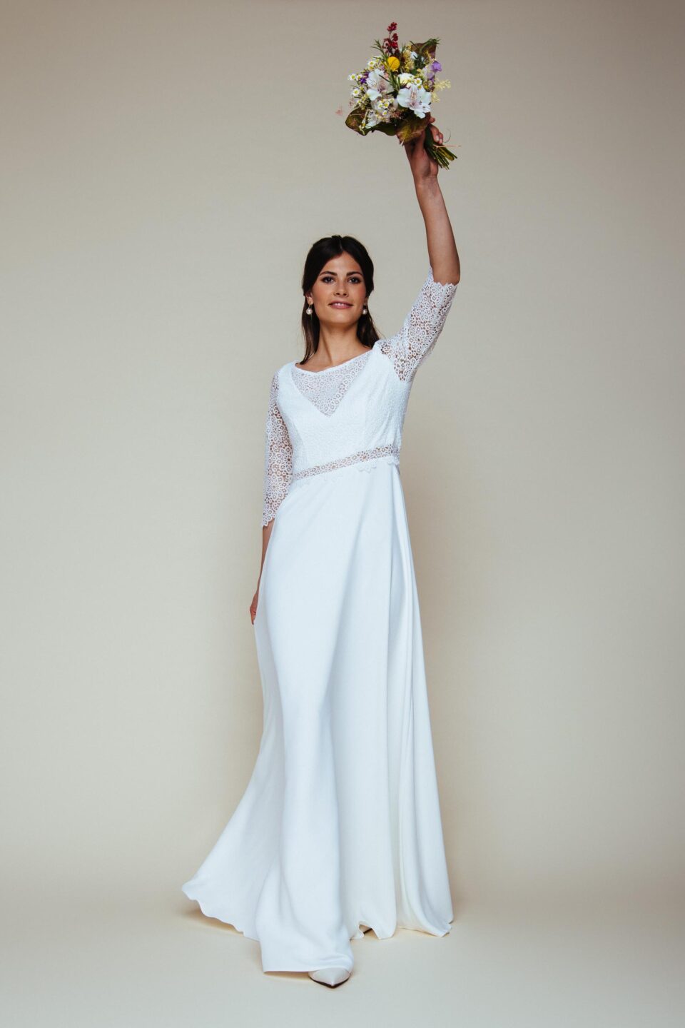 Braut hält Brautstrauß nach oben und trägt ein Brautkleid mit Spitze am Ärmel