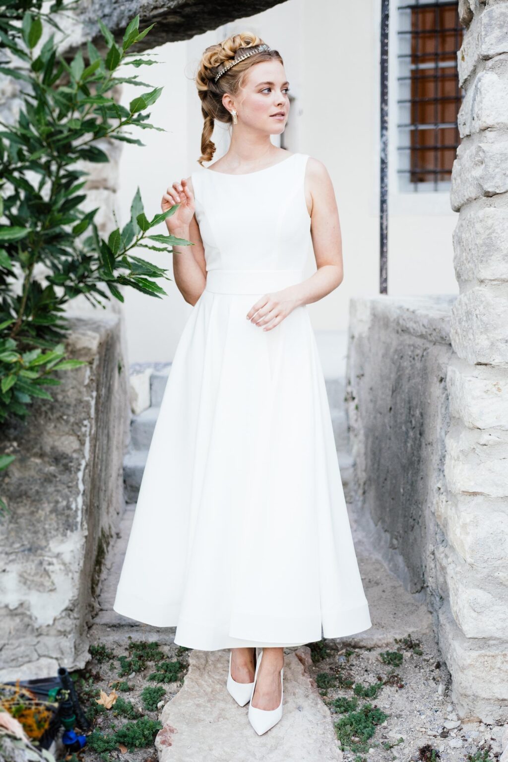 Braut im knöchellangen Kleid mit Brautstrauß vor einer alten Steinmauer