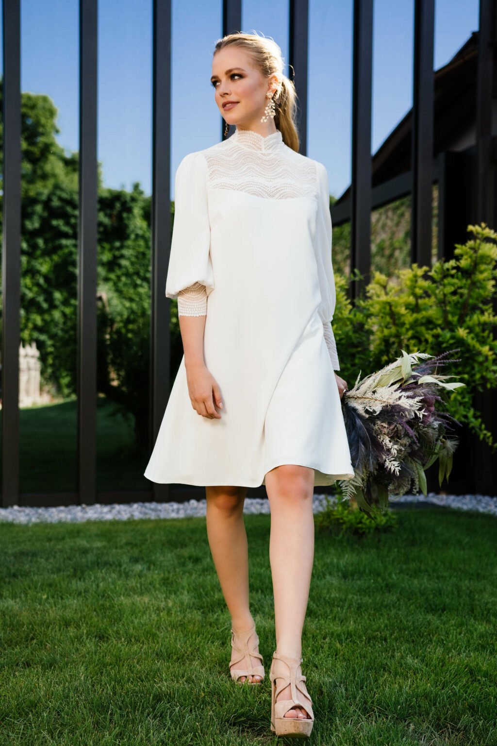 Braut im kurzen Kleid mit Stehkragen und Ballonärmeln im Garten