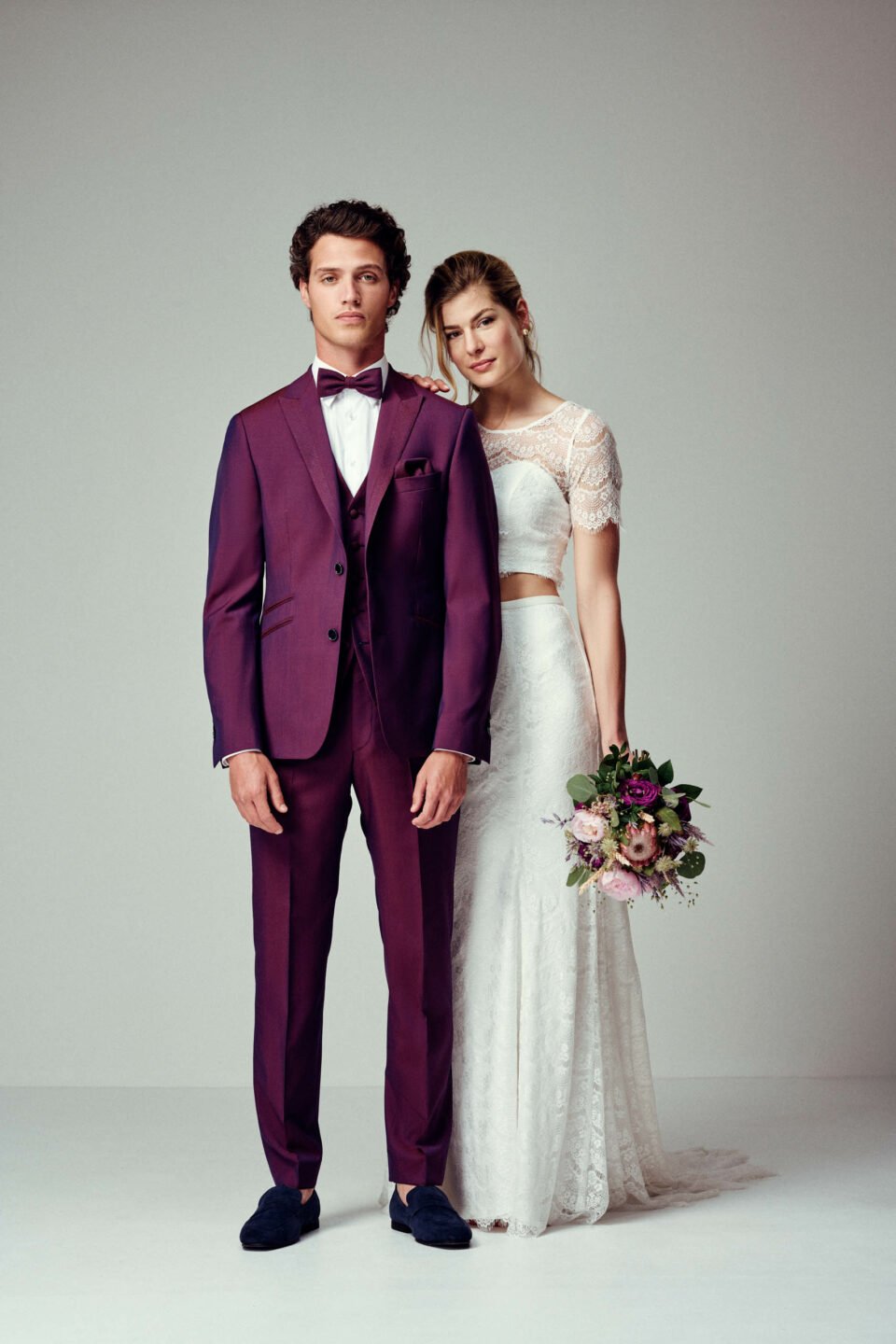 Braut im bauchfreien Zweiteiler neben Bräutigam im Rot-Blauen Anzug in Two-Tones Optik