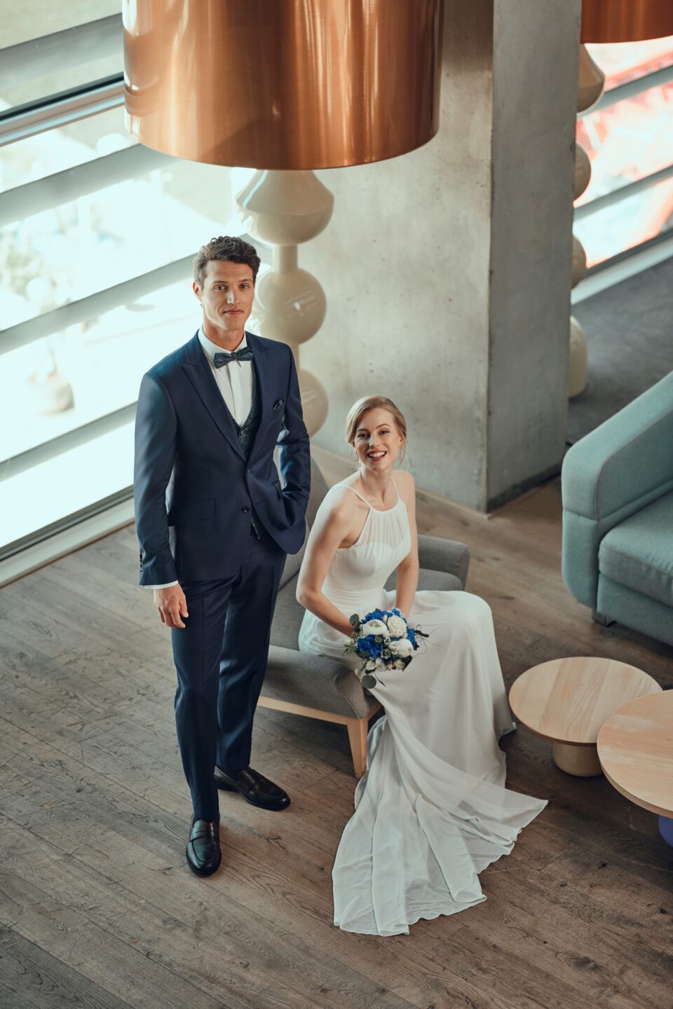 Bräutigam steht neben der sitzenden Braut im schlichten Brautkleid