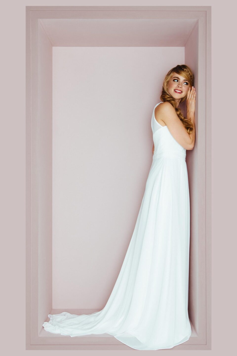 Braut lehnt sich im schlichten Hochzeitsklei an die Wand
