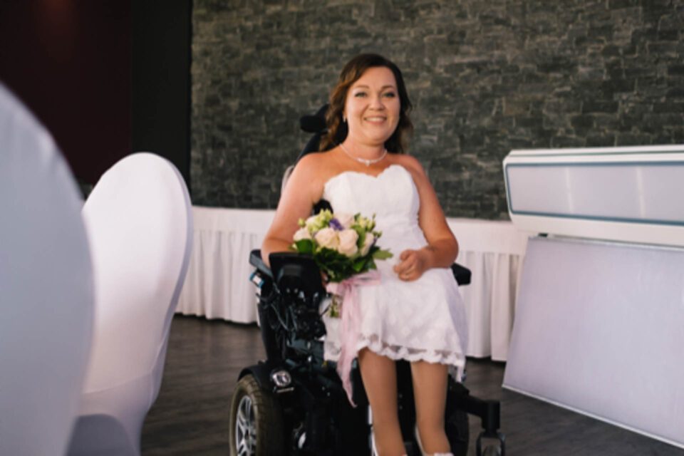 Braut im Rollstuhl im kurzen Brautkleid mit Brautstrauß