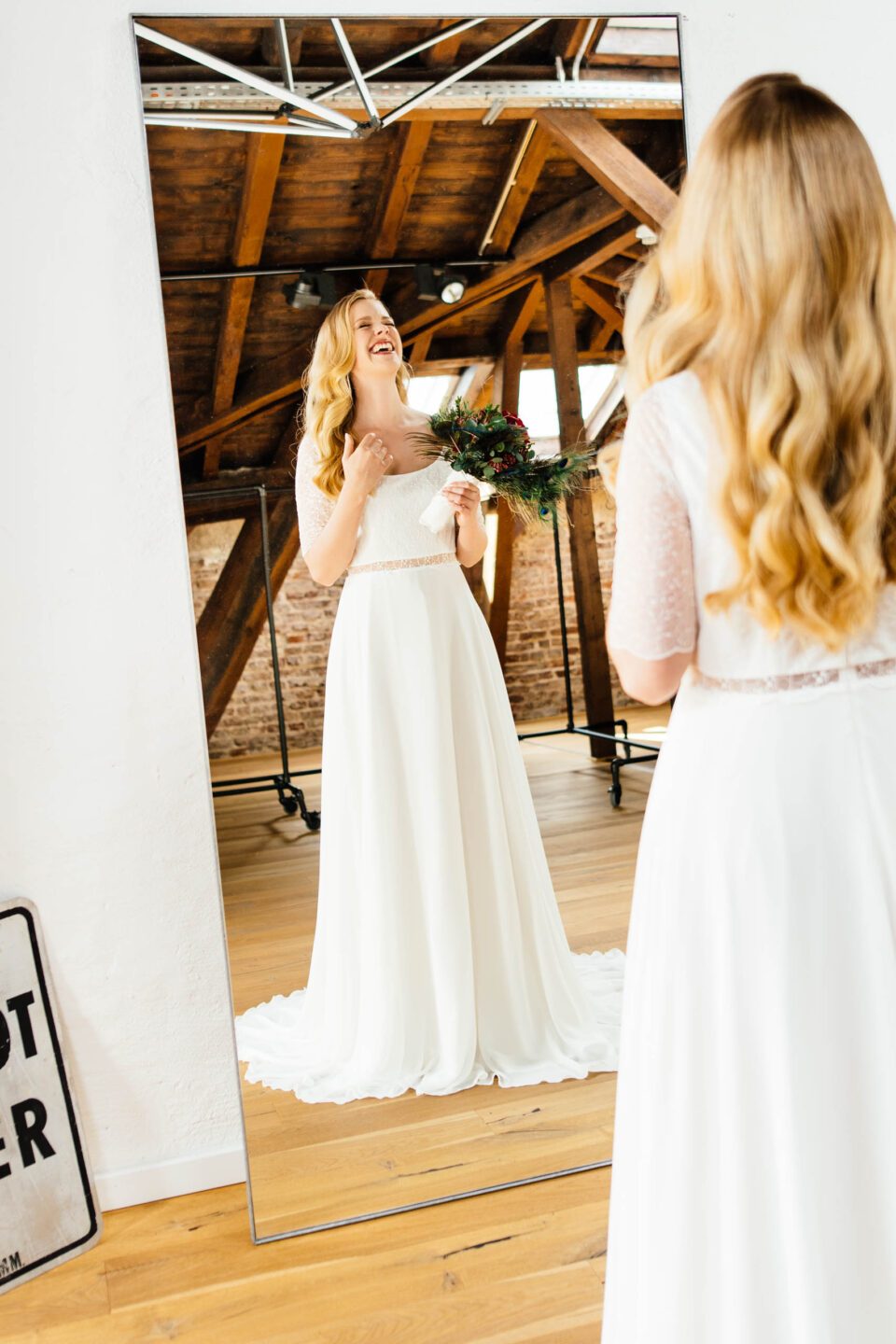 Braut lacht vorm Spiegel im Brautkleid mit Rundhalsausschnitt 