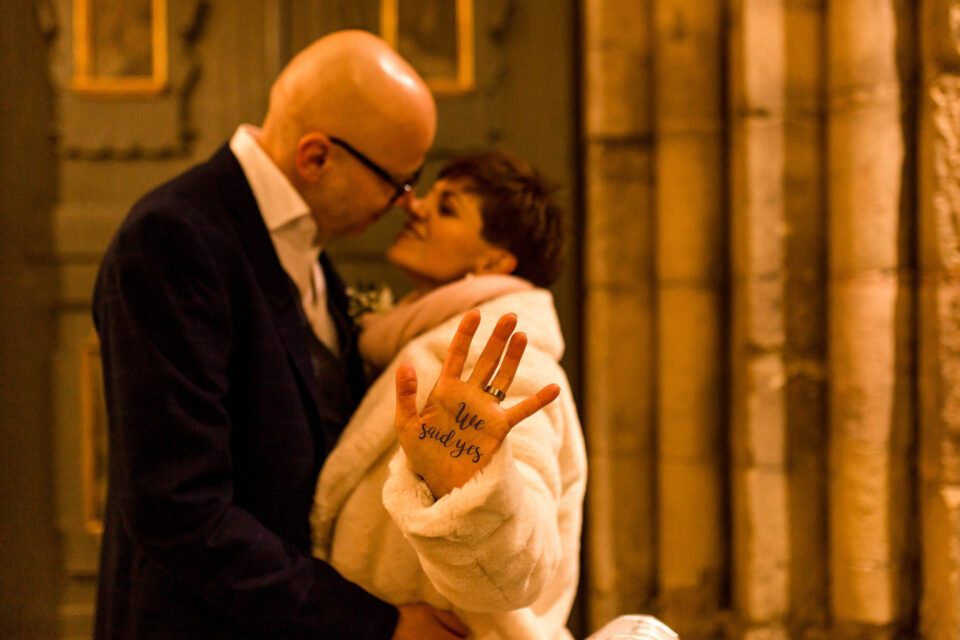 Dezmemberbraut mit Brautmantel hält Hand mit Aufschrift "we said yes" in die Kamera