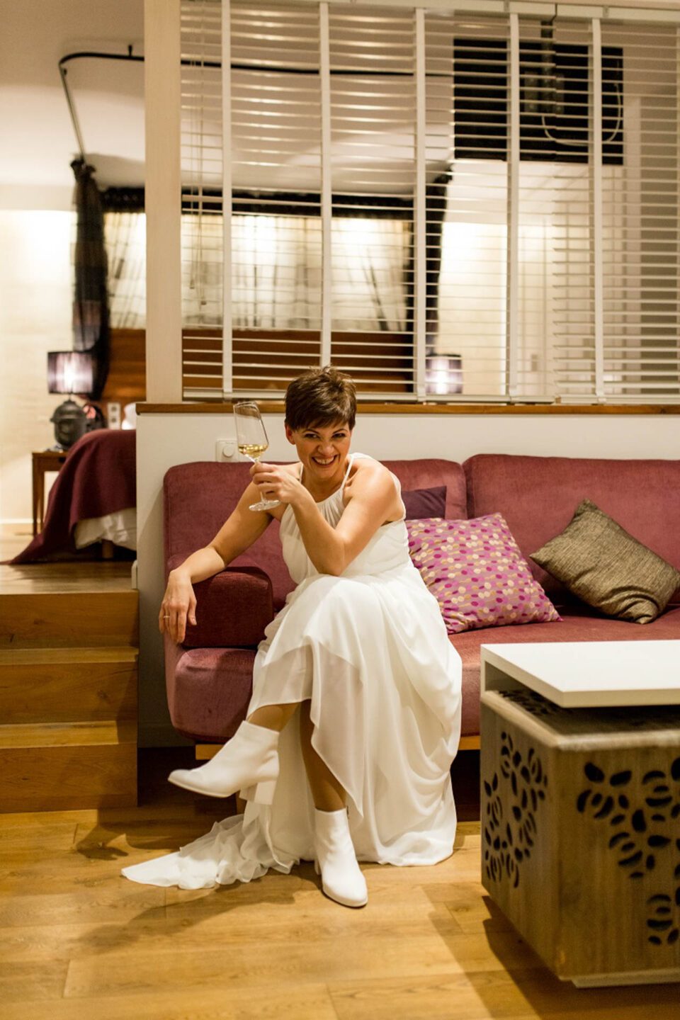 Lachende Braut mit einem Glas Weiswein auf dem Hotelzimmer