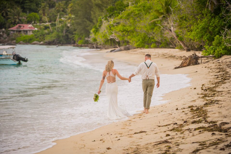 Brautpaar von hinten spazierend am Sandstrand nach Trauung auf den Seychellen