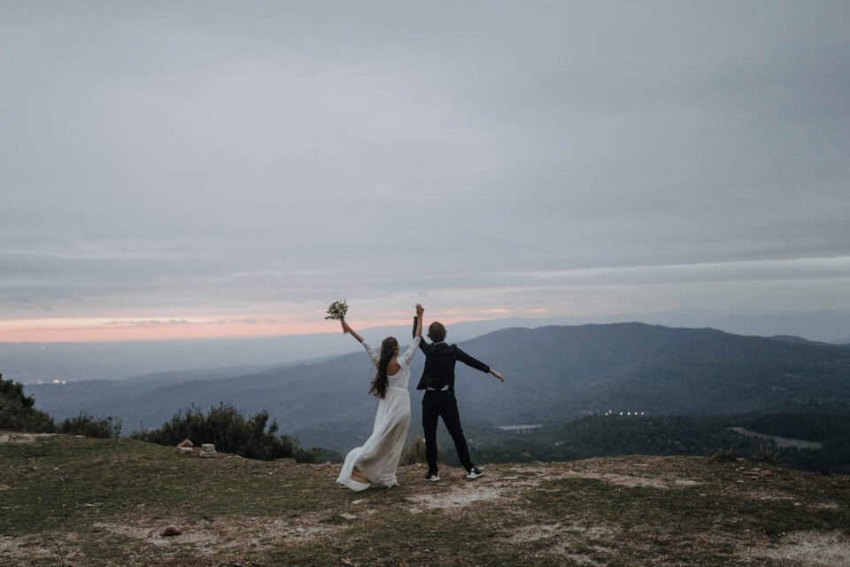 Brautkleid Zweiteiler in Spanien - Brautpaar streckt die Arme in den Himmel auf der Gebirgskette Montserrat