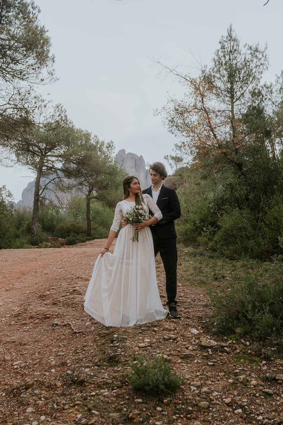 Brautkleid Zweiteiler in Spanien an schöner Braut, die vor dem Bräutigam steht und ihn über dei Schulter anlächelt