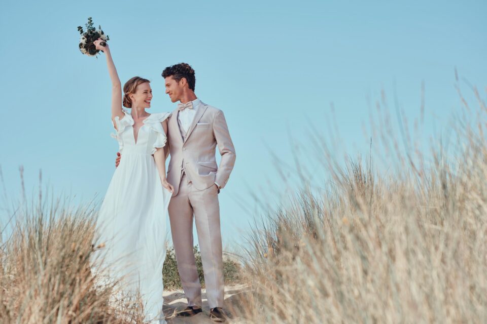 Brautpaar in den Dünen, Braut streckt Arm mit Brautstrauß fröhlich nach oben