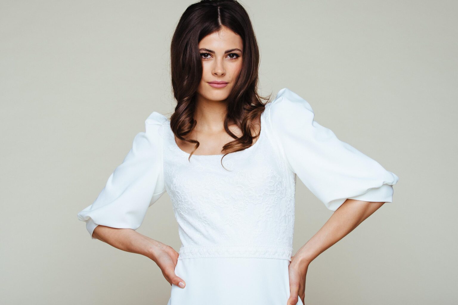 Braut im schlichten Kleid mit voluminösen Puffärmeln, die Hände in die Hüften gestützt