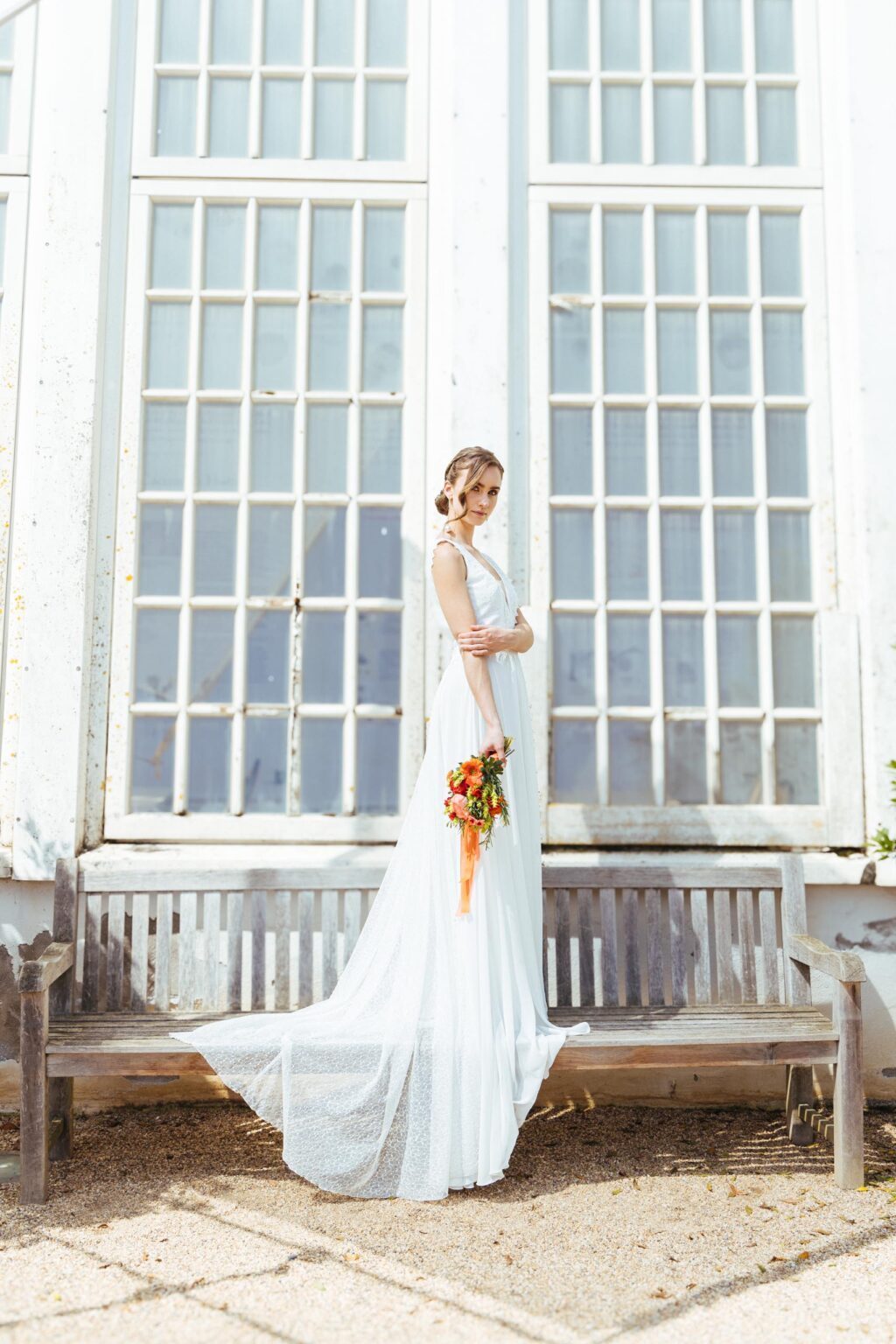 Braut im Brautkleid KUESSdieFIRENZE mit Spitzenoberteil und Chiffonrock vor einem Gewächshaus