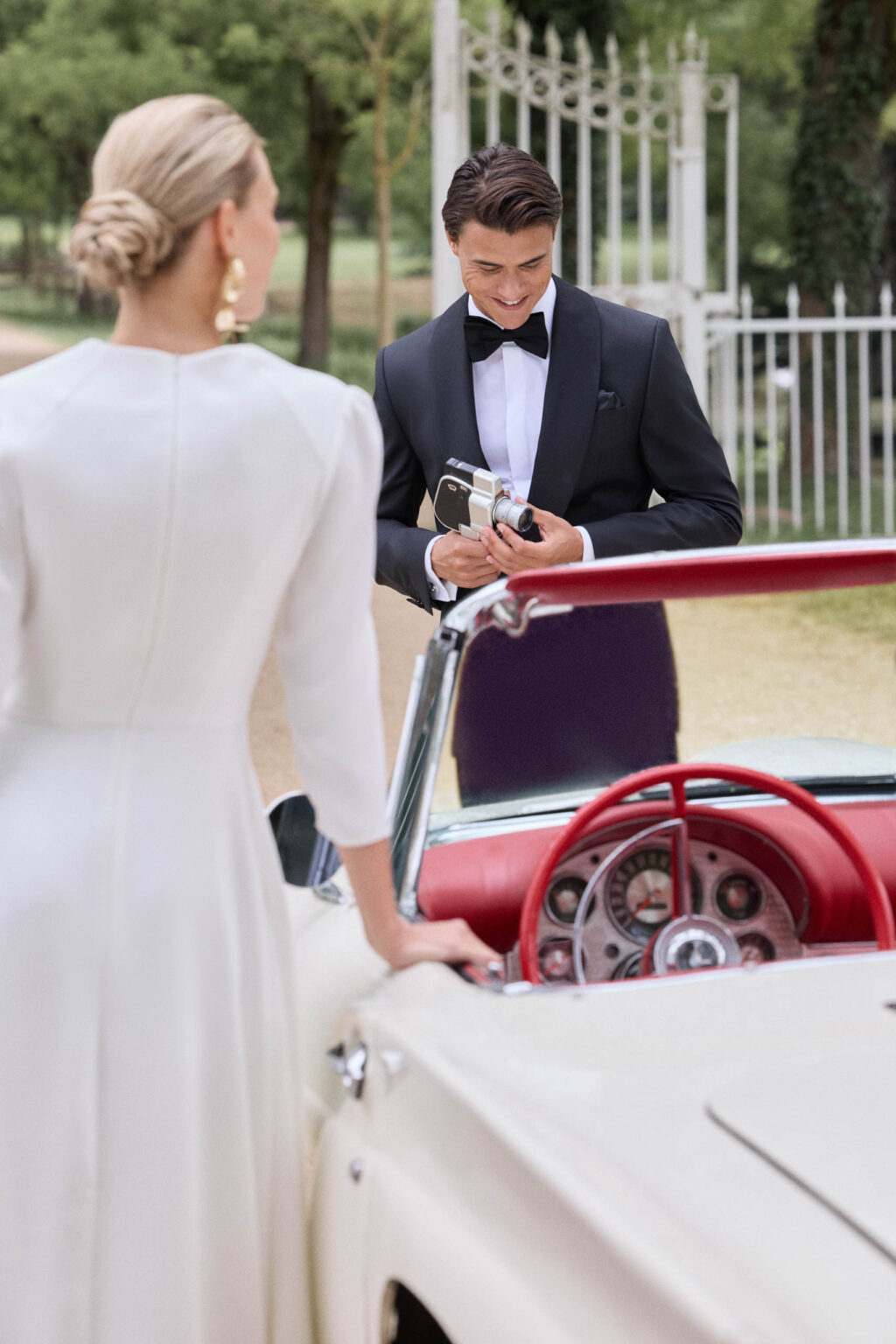 Bräutigam im schwarzen Smoking an einem weißen Oldtimer, Braut im Kleid mit 3/4-Arm