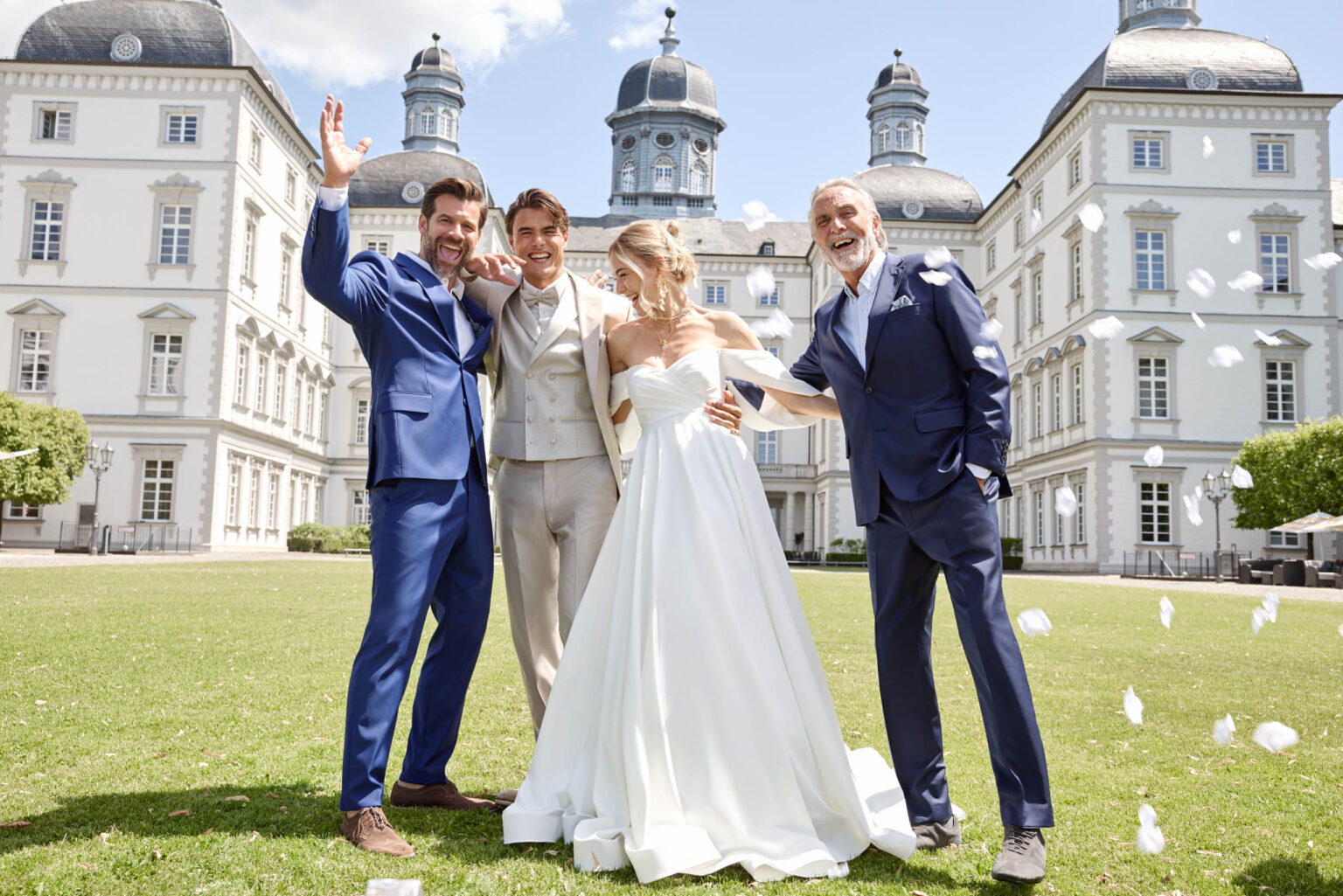 Brautpaar mit zwei Männern in blauen Anzügen vor einem Schloss