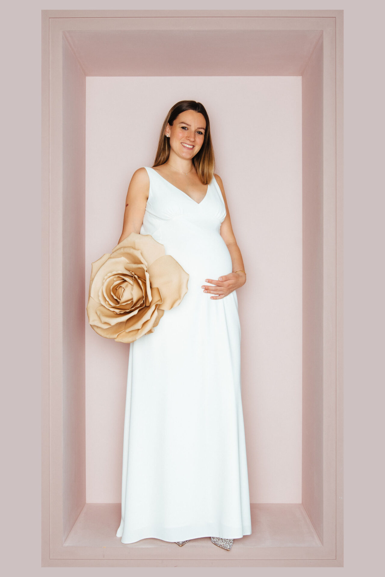 Schwangere Braut im ärmellosen V-Ausschnitt-Brautkleid aus Chiffon, im Arm eine große Papierrose