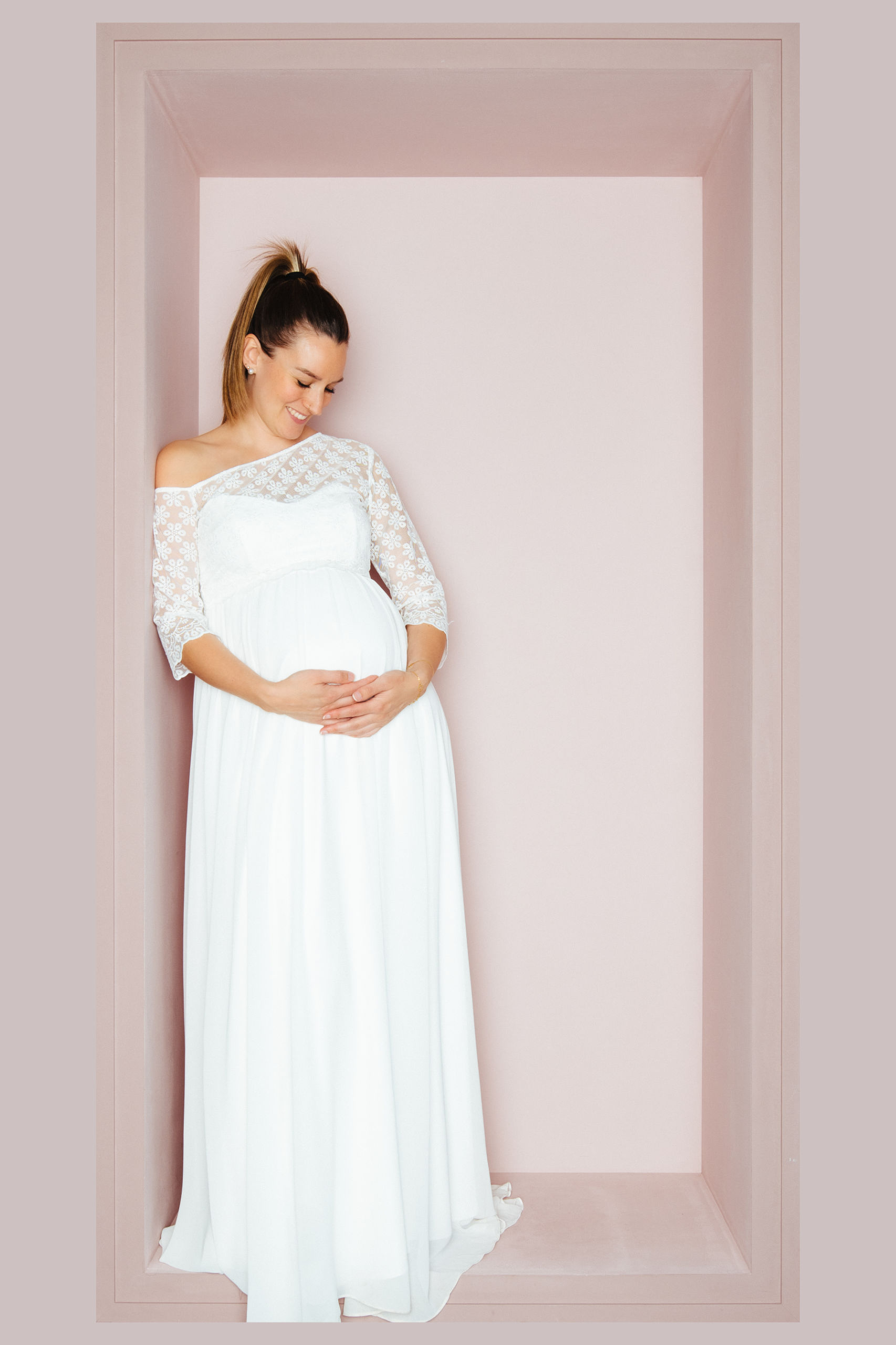 Schwangere Braut in elegantem One-Shoulder Brautkleid mit Spitzenärmel und Empire-Linie von KUESSdieBRAUT