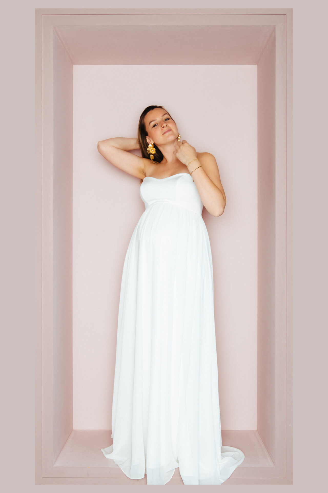Schwangere Braut im trägerlosen Chiffon-Brautkleid mit Empire-Taille, eine Hand im Haar