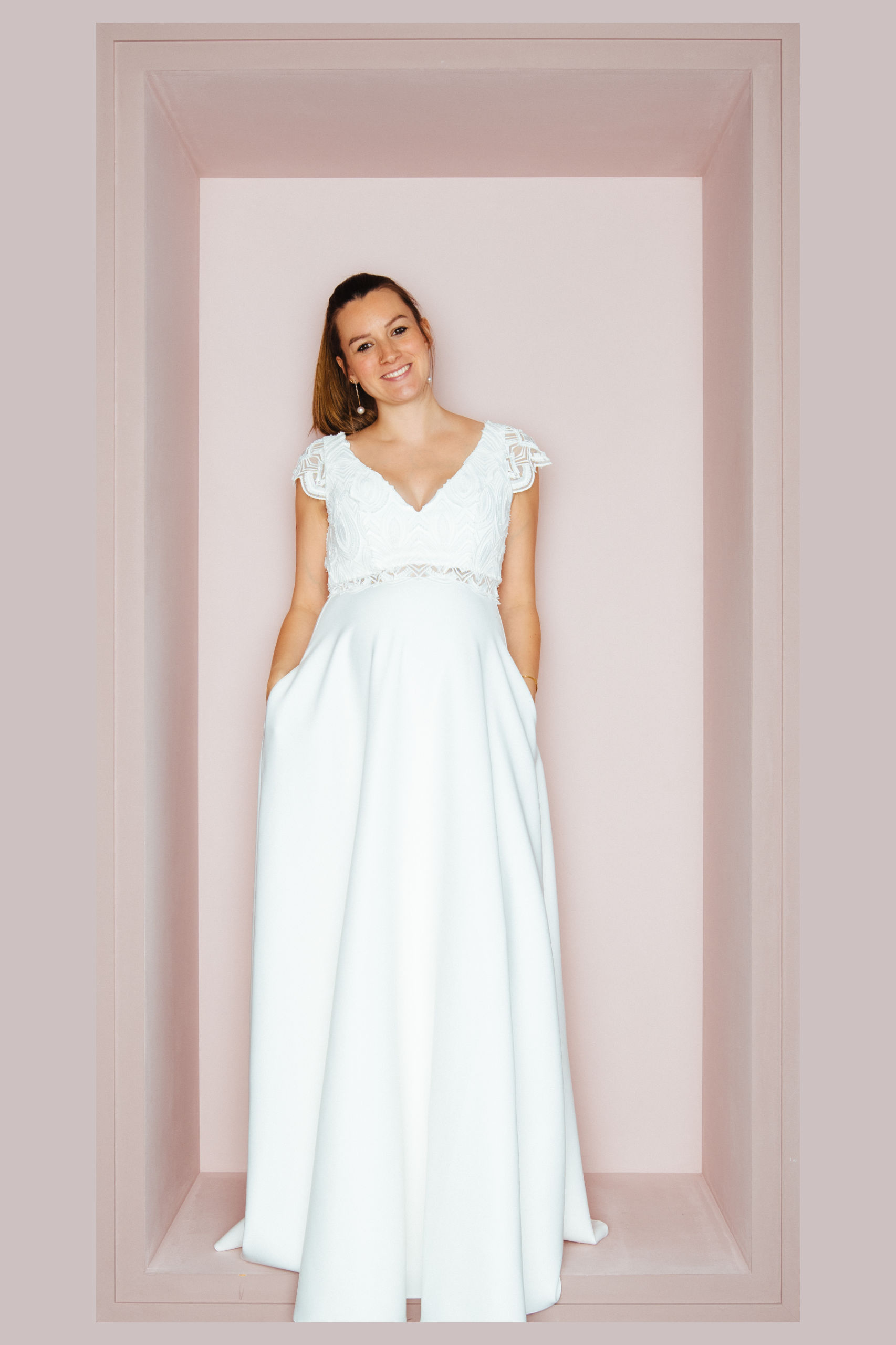 Schwangere Braut in glamourösem weißem Halterneck-Brautkleid FONTE mit Beinschlitz und Strass-Gürtel von KUESSdieBRAUT
