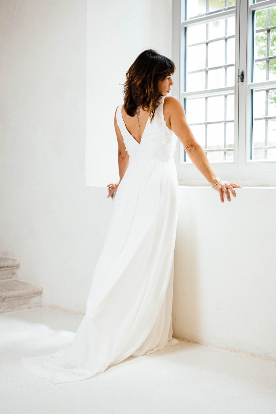 Brautkleid KUESSdieBIBBONA mit ausgeschnittenem Spitzenrücken und kleiner Schleppe, Rückansicht am Fenster